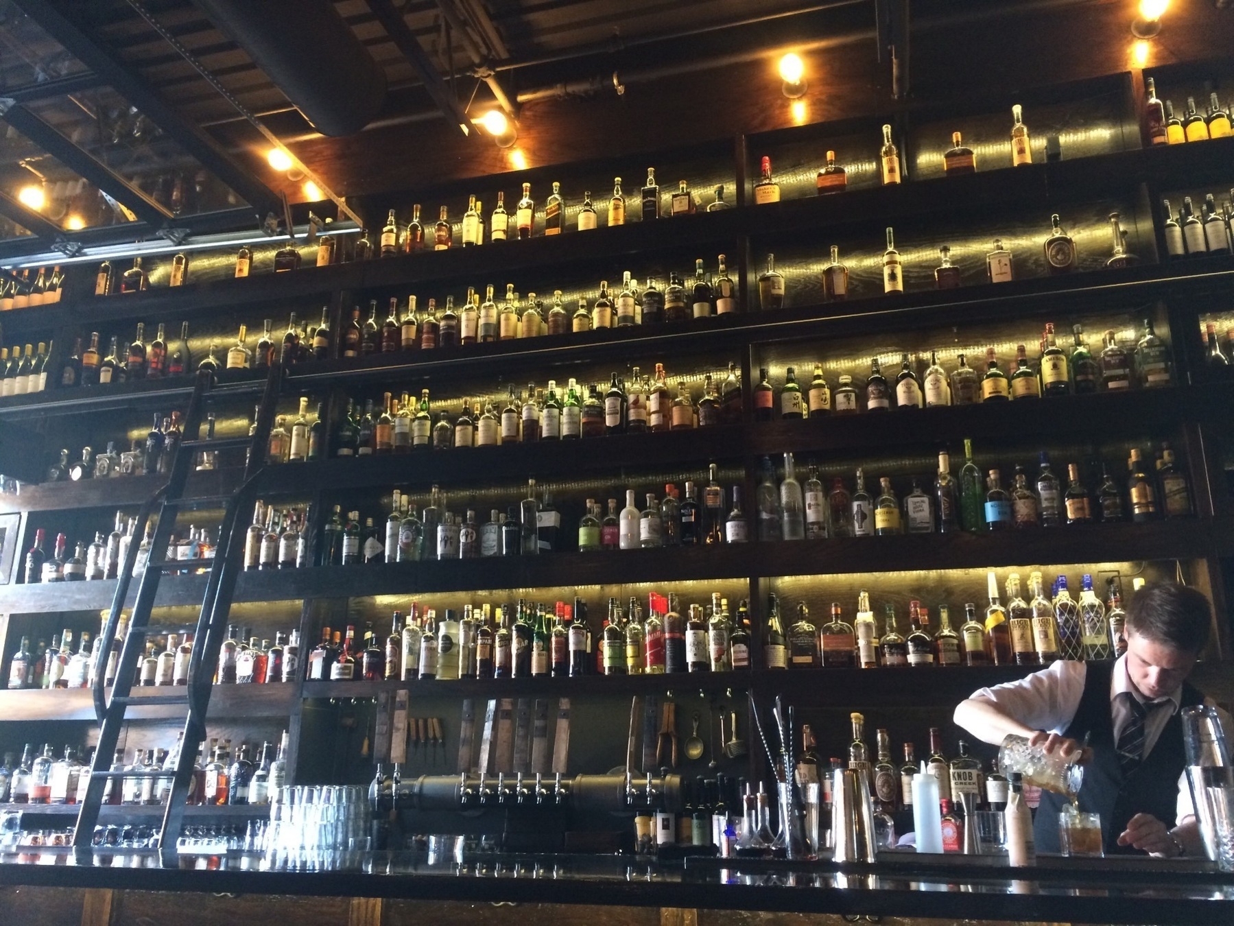 A wall of liquor bottles behind a bartender mixing a drink