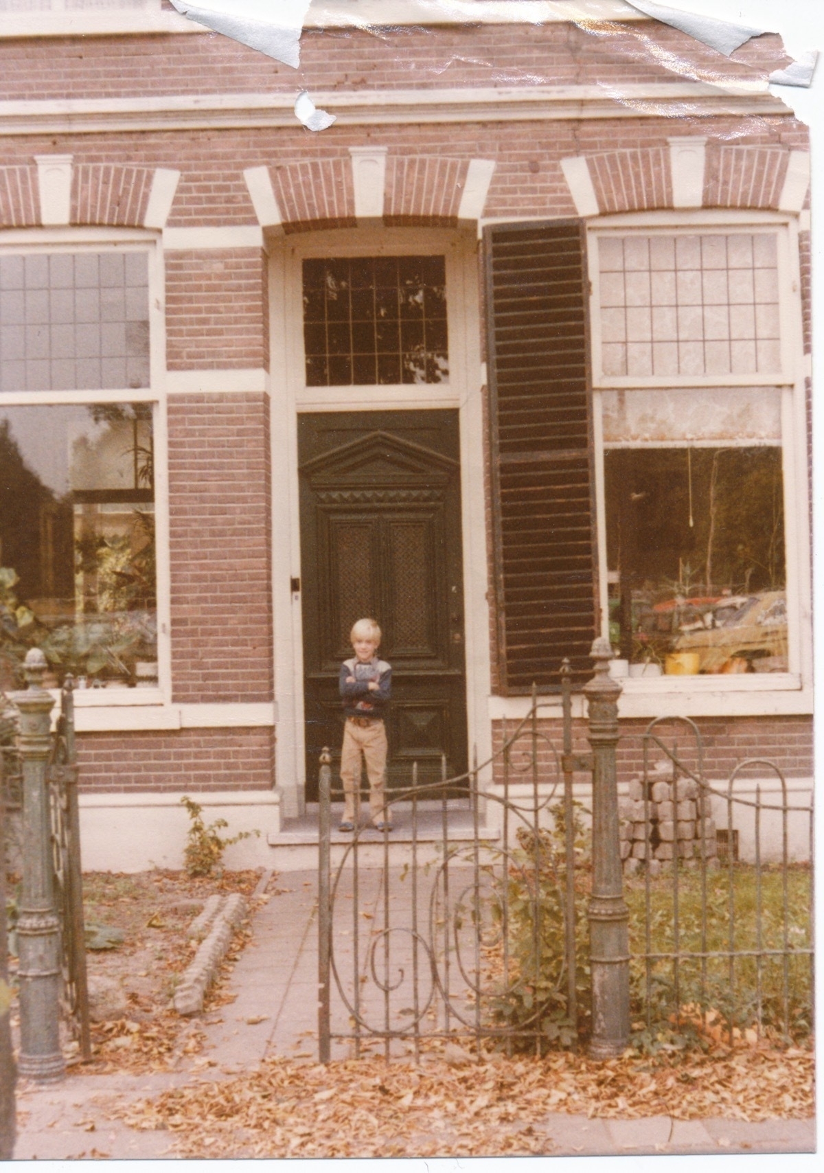 The front of a brick house in the Netherlands in 1977 with me, aged 7, standing at the front door
