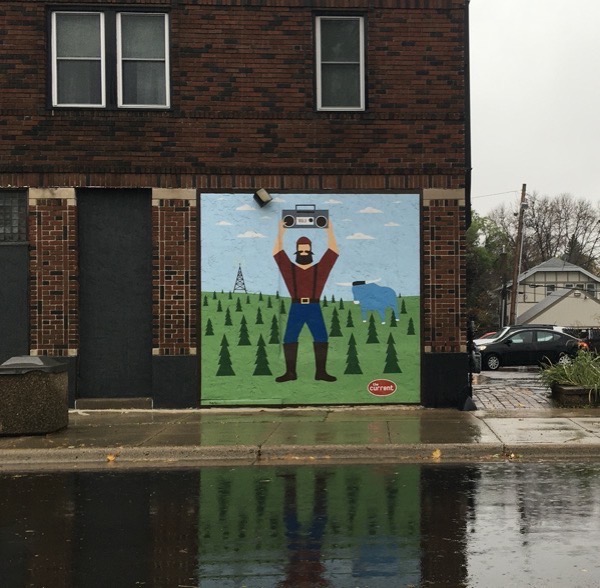 A mural on the side of a building for The Current, a Twin Cities radio station: Paul Bunyon standing with a boombox over his head, like Lloyd Dobler in Say Anything. Babe the blue ox is nearby, a radio tower is in the distance